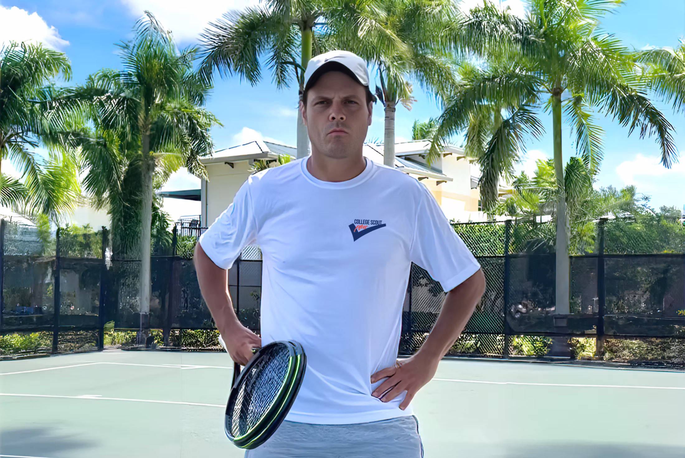 Marcus Schneider stands on an outdoor tennis court in a white shirt and cap, holding a racket — Boca Raton, Florida.