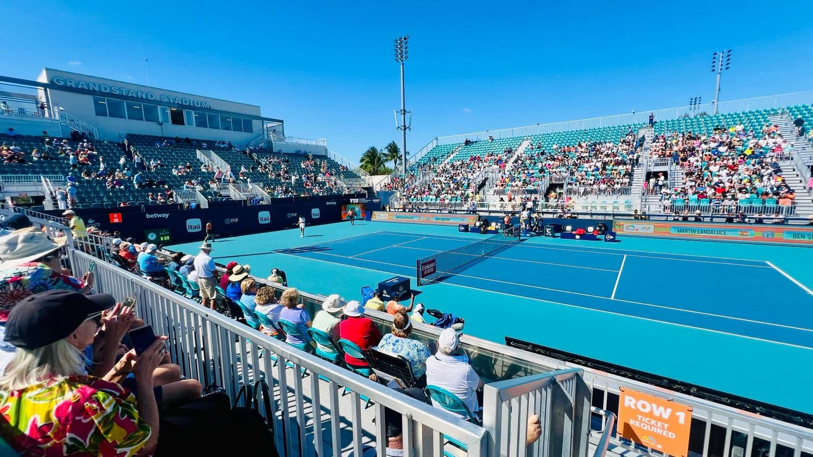 Tennis match on a blue court with stands and spectators.