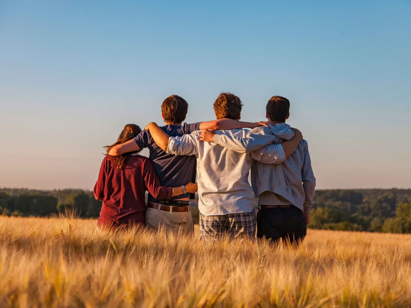 Four friends with arms around each other in a field at sunset.