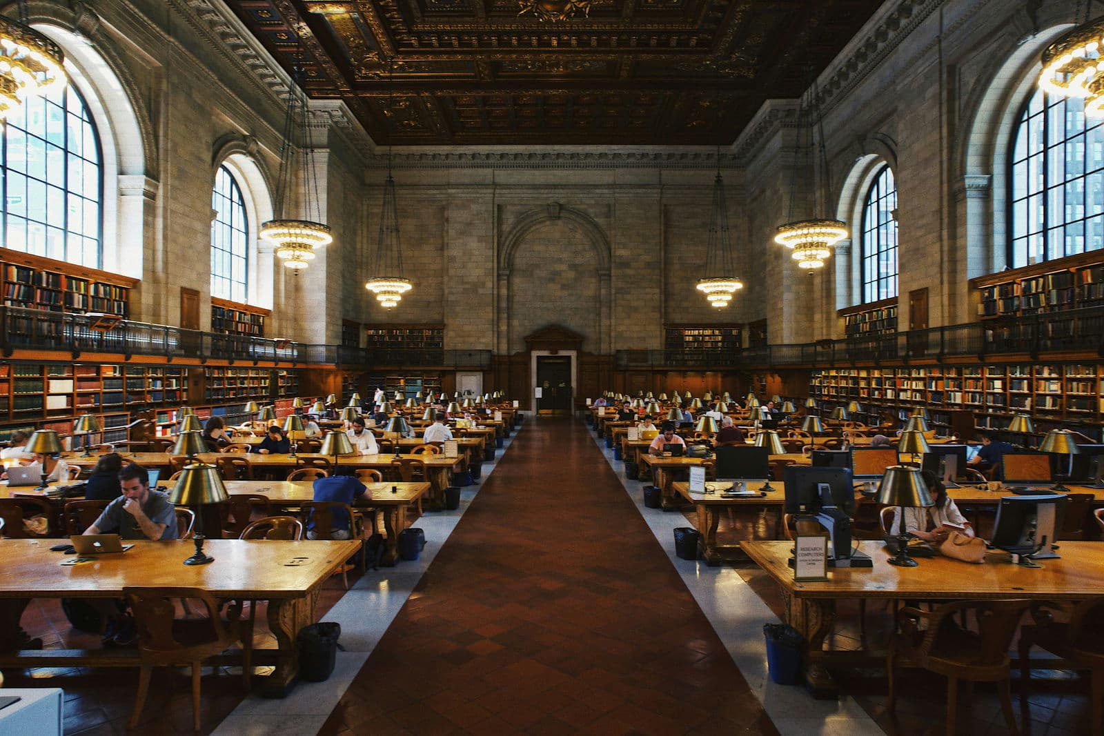 Bibliotheksähnlicher Lesesaal mit antiken Tischen voller Bücher — Symbol für akademisches Umfeld.