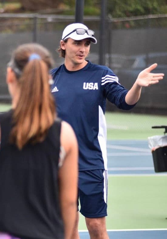 Trainer erklärt einer sportlich gekleideten Spielerin auf dem Tennisplatz die nächste Übung.
