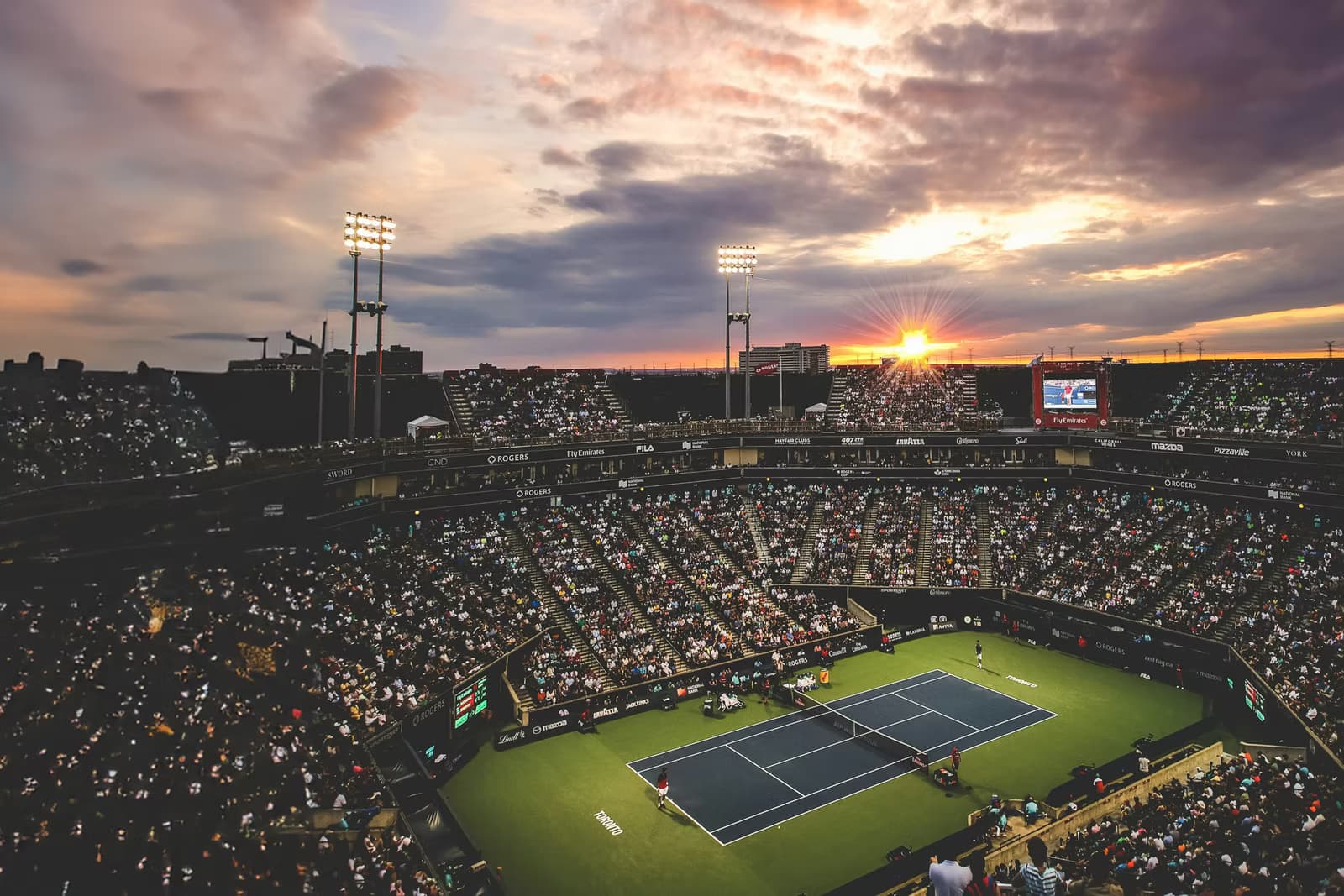 Tennisstadion zur Abendstimmung mit Zuschauern und Flutlicht über dem Spielfeld.