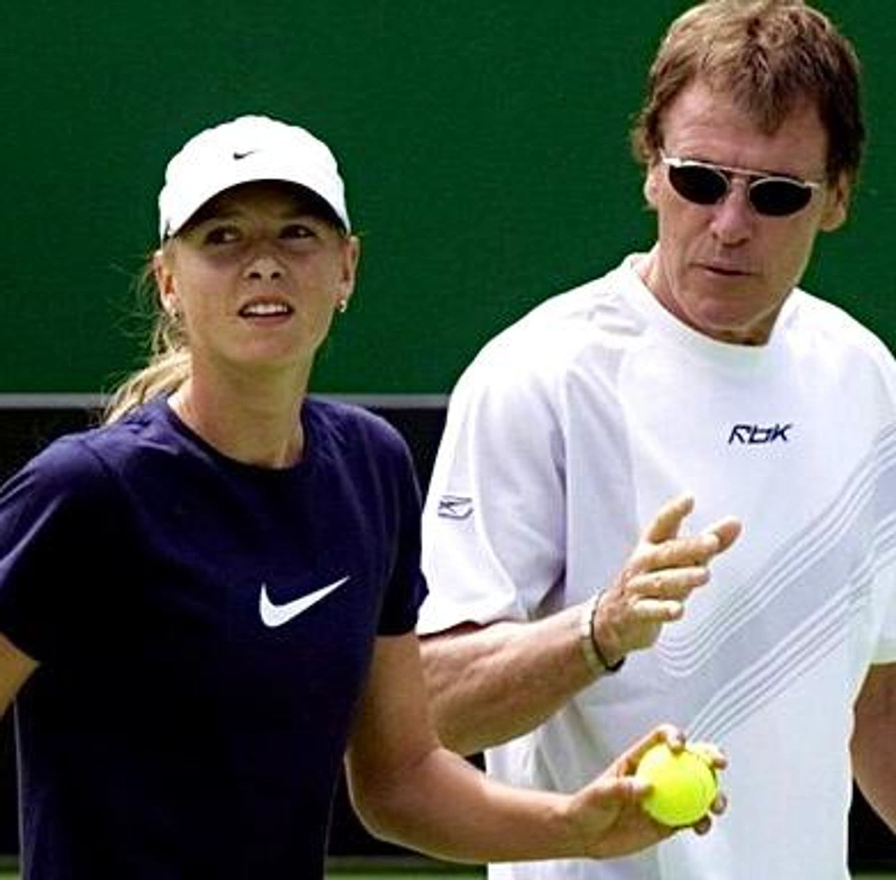 Coach und Spielerin auf einem Tennisplatz beim Technik-Gespräch — grüner Hintergrund hinter der Grundlinie.