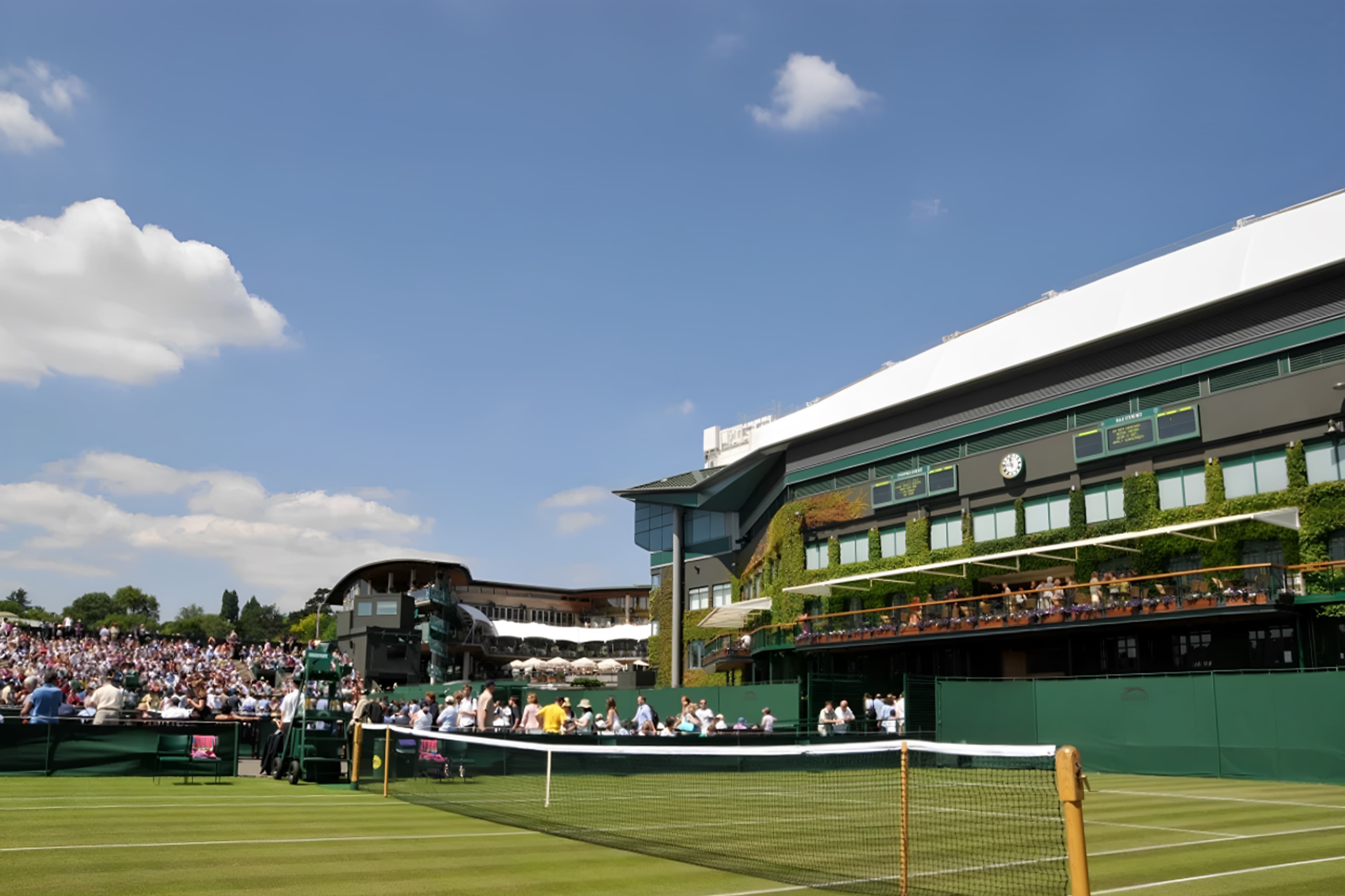 Wimbledon — a fully packed tennis stadium with a large crowd, alongside a building with a roof terrace
