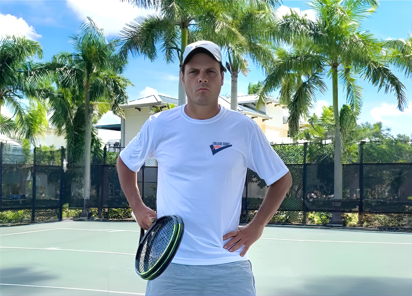 Marcus Schneider in a red shirt and cap on an outdoor tennis court with palm trees.