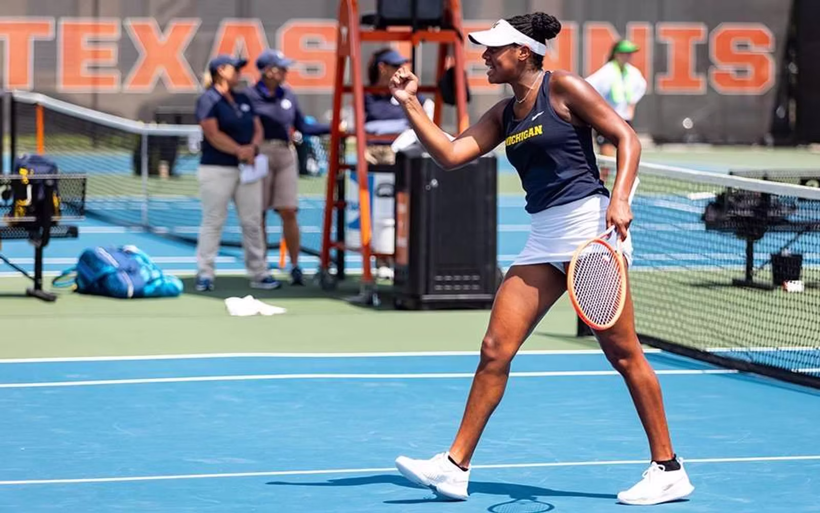 College tennis player celebrating on a blue hard court.
